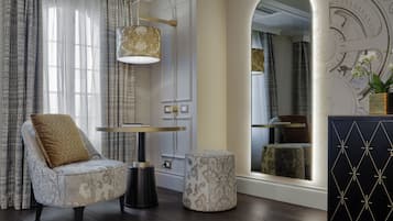 Una sala moderna con un sillón estampado, un otoman redondo, una lámpara de pie y un aparador decorativo.