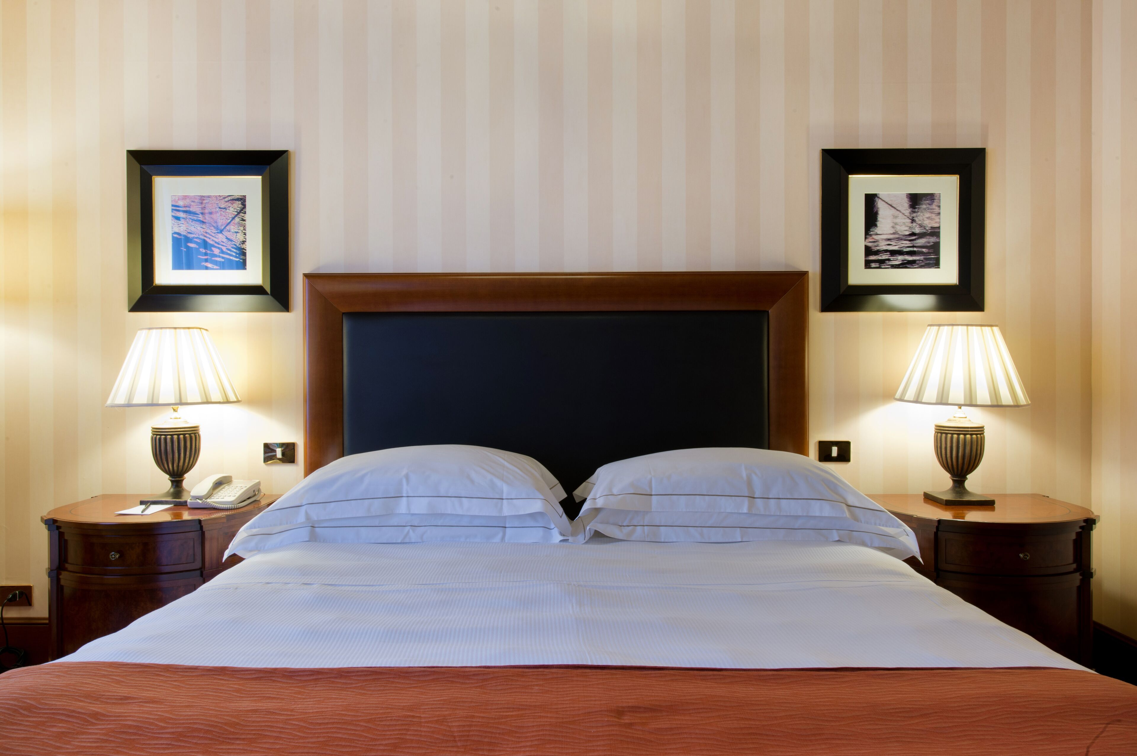 Un cuarto de hotel con una cama grande, dos mesitas de noche con lámparas, y cuadros enmarcados en las paredes.