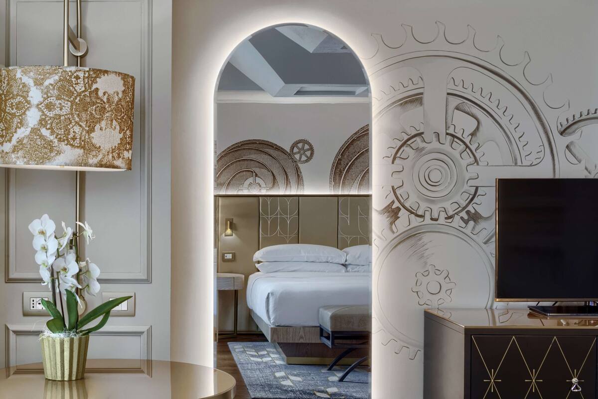 Une chambre d’hôtel moderne avec un lit, une télévision, un mur décoratif et un vase rempli de fleurs.