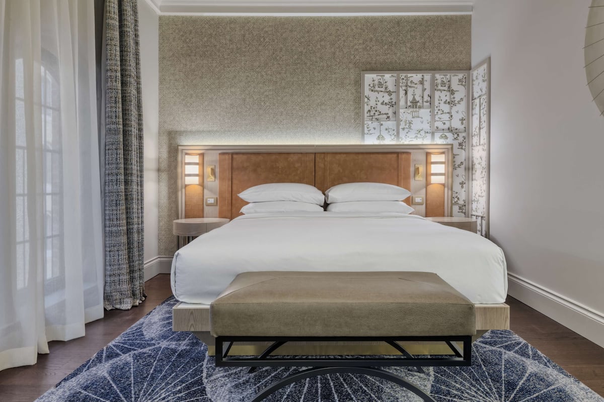 Une chambre à coucher bien aménagée, avec un grand lit, des lampes de chevet, un banc et un tapis à motifs.
