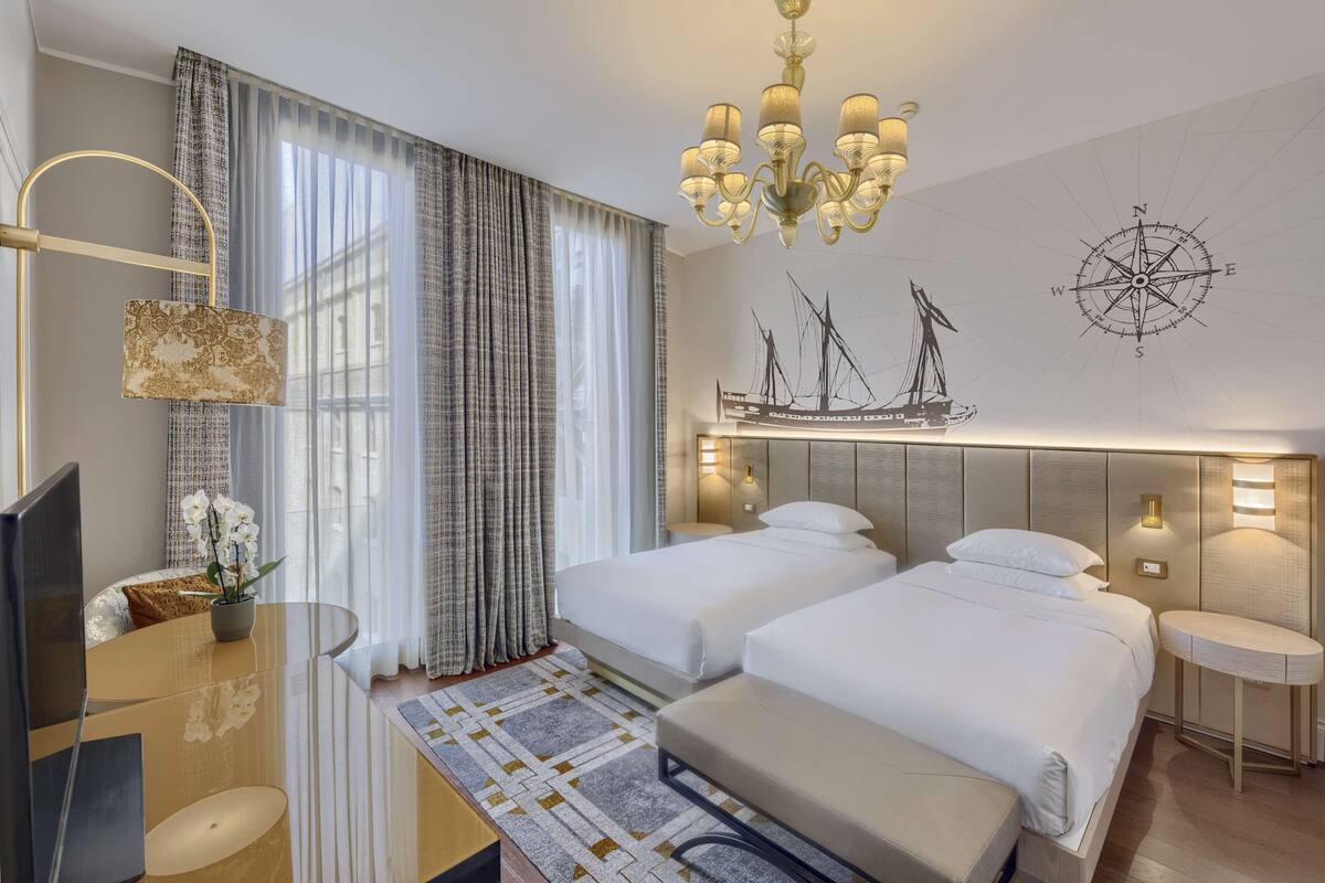 Une chambre d’hôtel avec deux lits, une télévision, un bureau, un lustre et une boussole fixée au mur.
