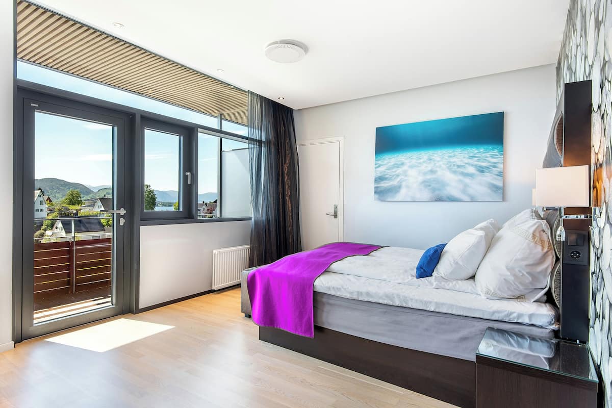 A modern bedroom with a bed, a large window, and a view of the outdoors.
