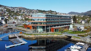 A modern building with a glass facade, situated by a marina with docked boats. - Quality Hotel Ulstein (Ulsteinvik)