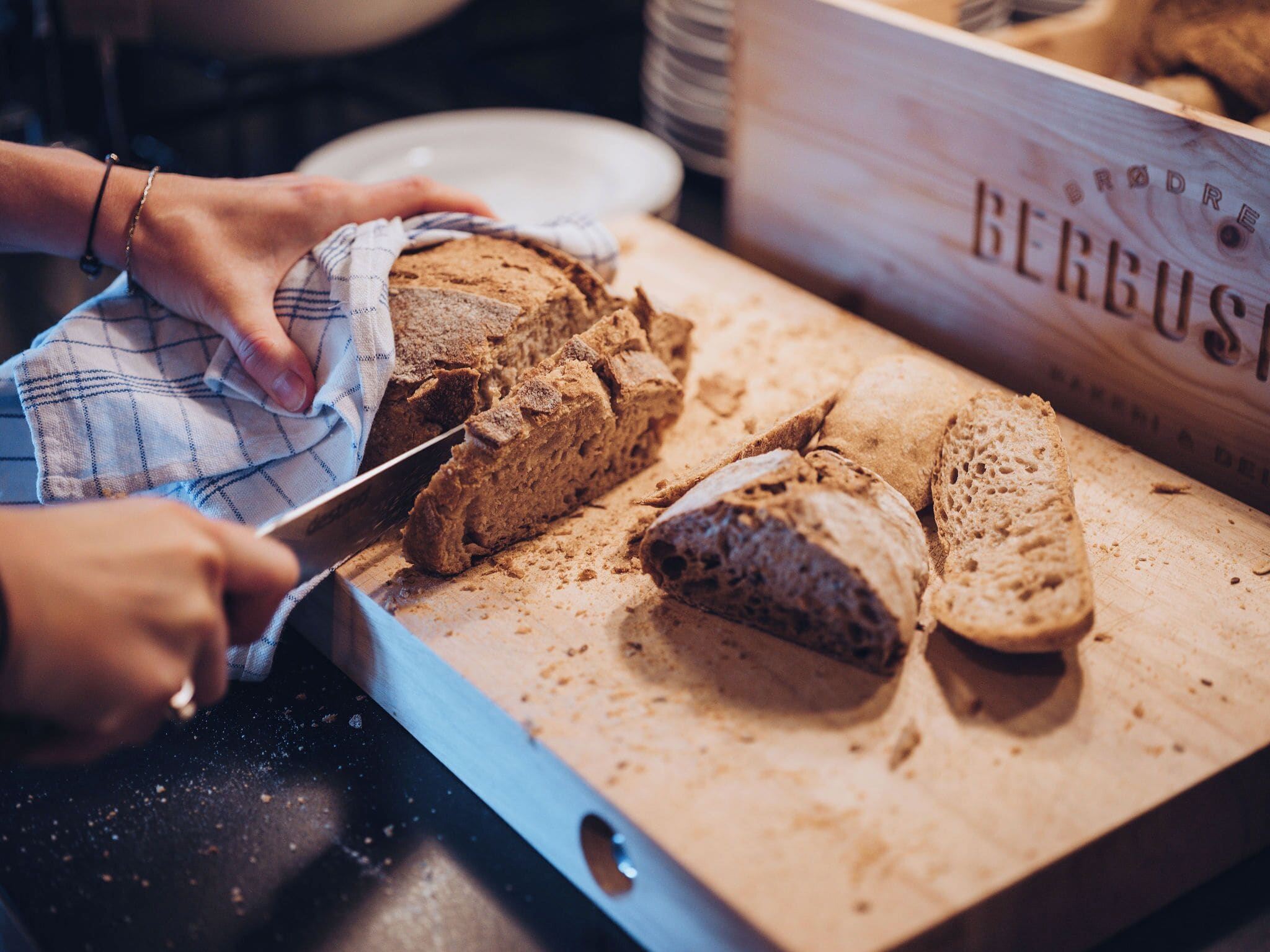 A person slicing a loaf of bread on a wooden cutting board.