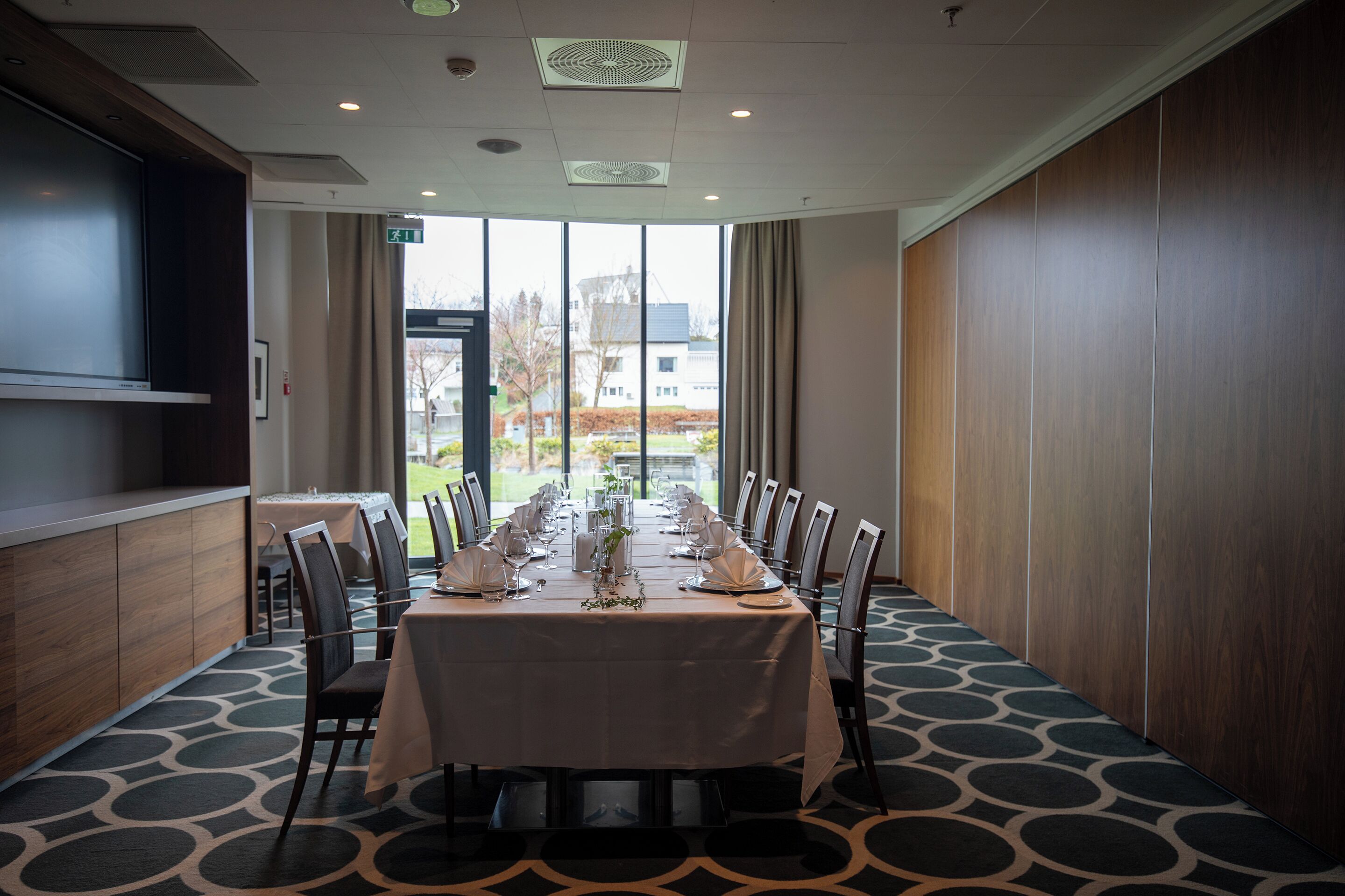 Un salón de conferencias con una larga mesa lista para una reunión, ventanas amplias y vistas al exterior.