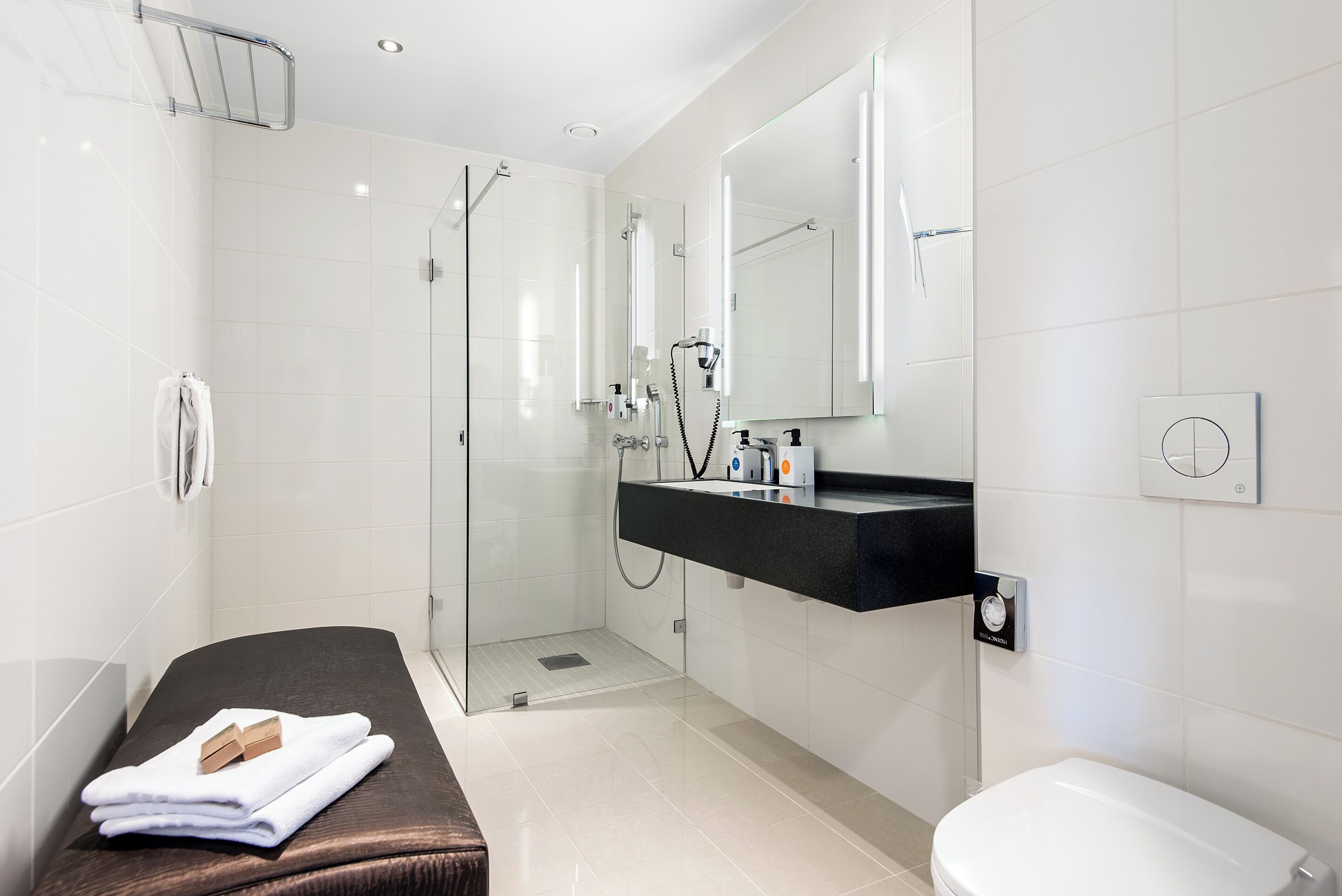 A modern bathroom with a glass shower enclosure, a black countertop with toiletries, and a white toilet.