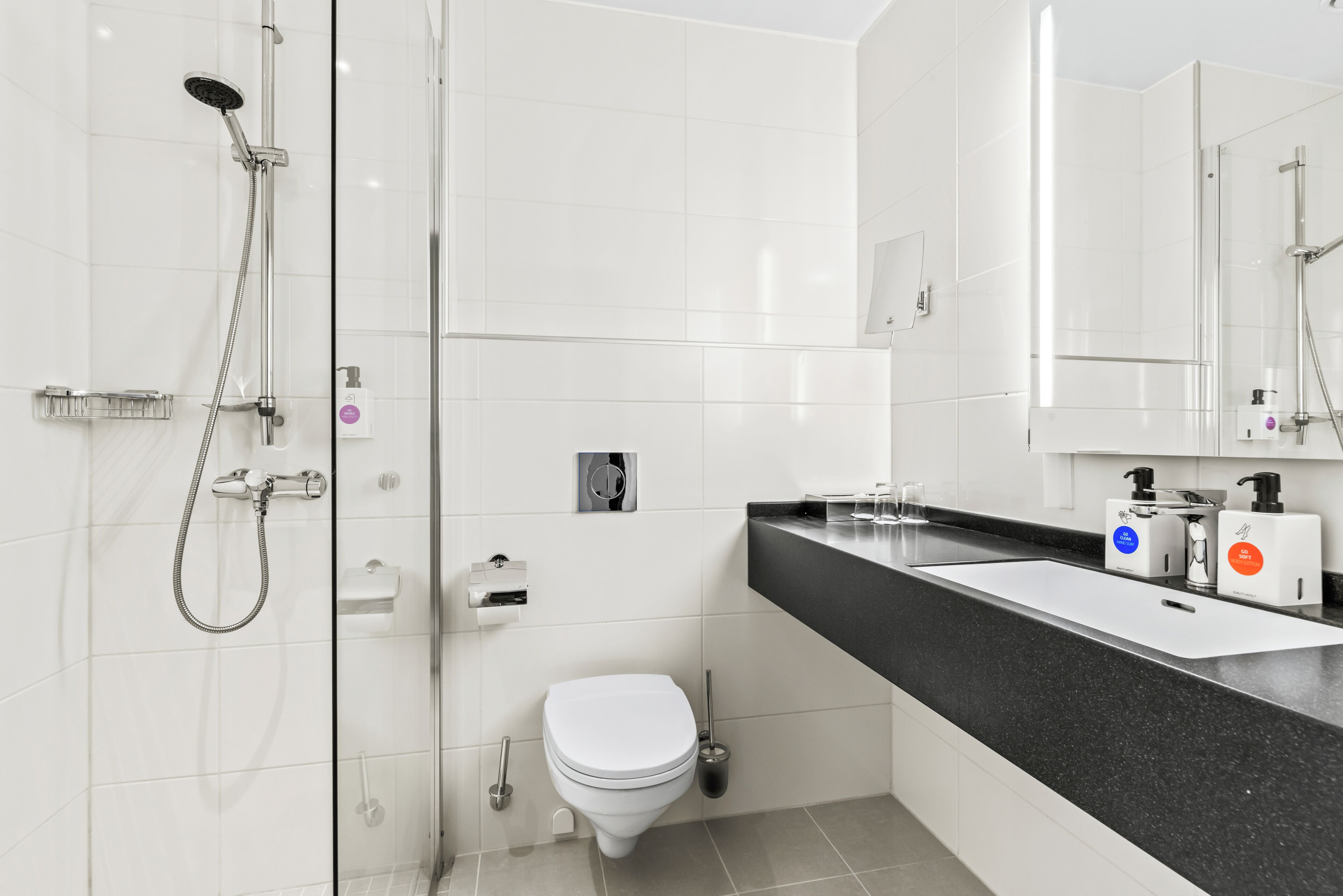 Ein modernes Badezimmer mit Duschkabine aus Glas, weißer Toilette und Waschbecken mit schwarzer Ablage und Seifenspendern.