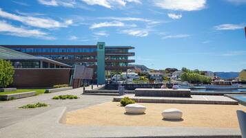 A modern building with multiple floors, a waterfront view, and a public square with seating areas.