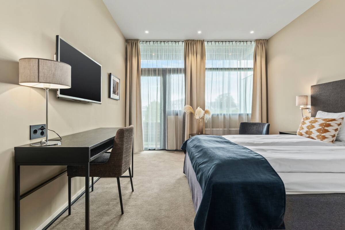 A hotel room with a bed, desk, chair, and a TV mounted on the wall.