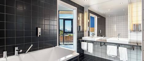 A modern bathroom with a large bathtub, two sinks, and a large mirror.