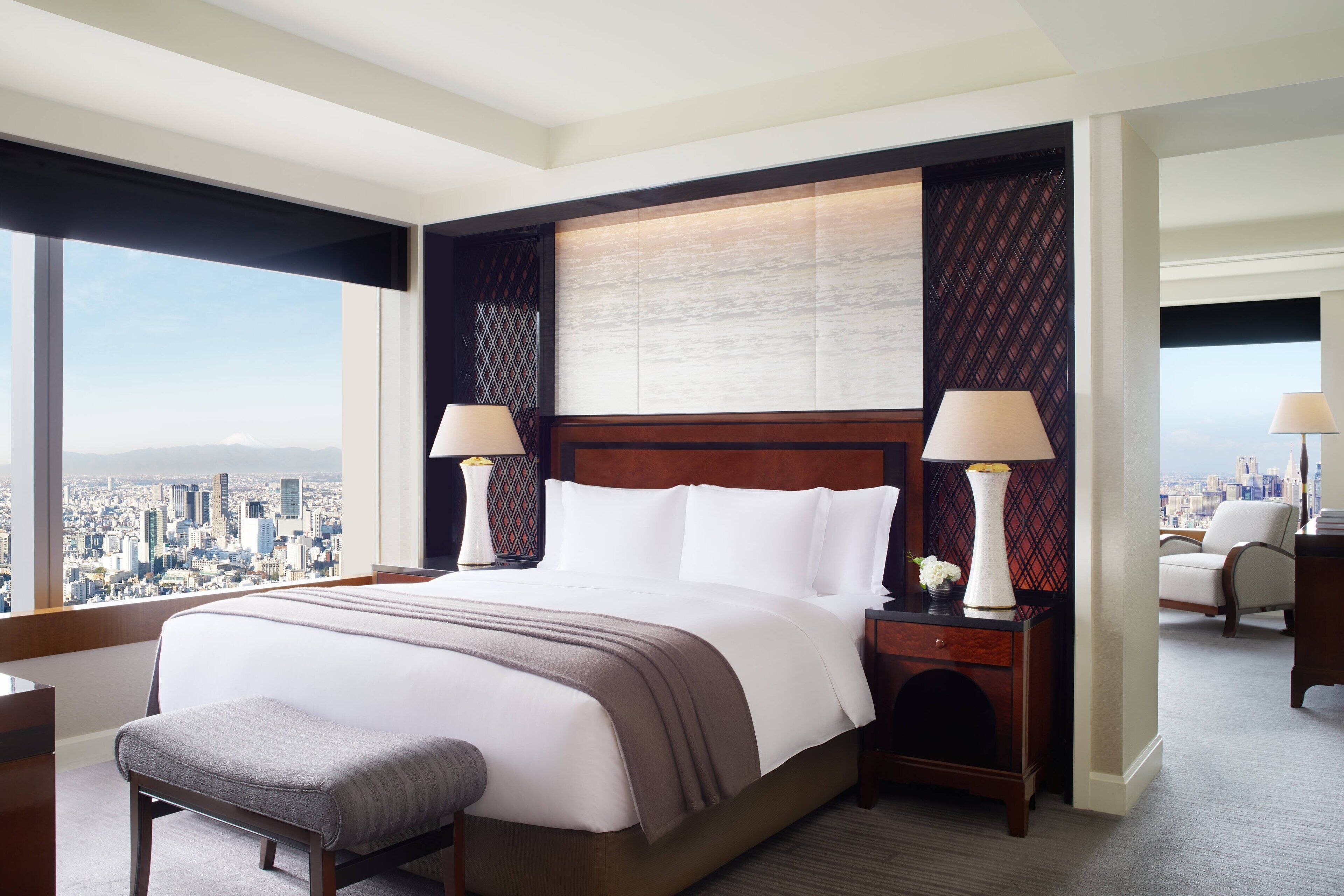 Une chambre d’hôtel avec un grand lit, deux tables de chevet avec des lampes, une vue sur la ville et un panorama urbain visible à travers de grandes fenêtres.