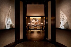 A hallway with a reception desk, two chairs, and a wall-mounted sculpture.