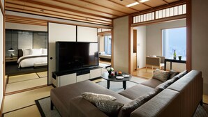 A modern hotel room with a sofa, television, and a dining area with a table and chairs.