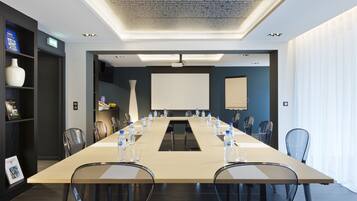 A modern conference room with a long table, chairs, and a projector screen.