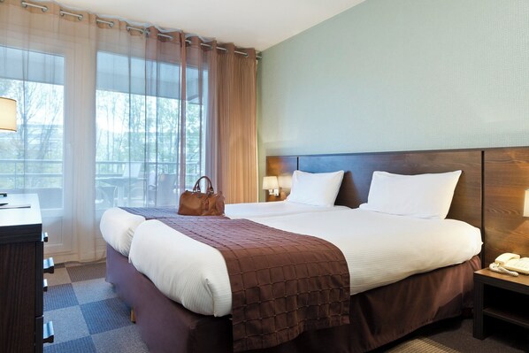 Habitación de hotel con una cama grande, una mesita de noche con lámpara, un escritorio con lámpara y una ventana con cortinas.