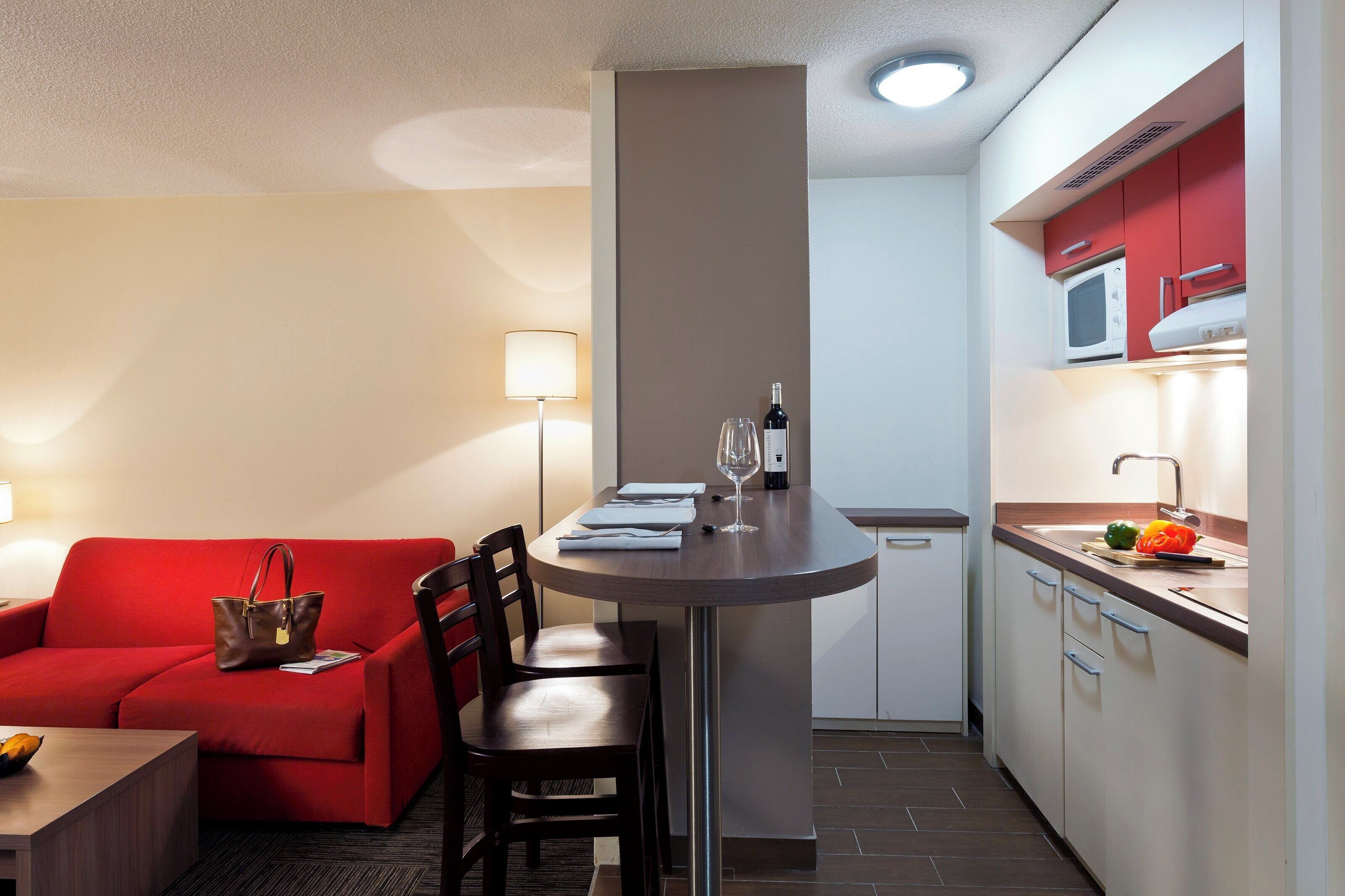 Una camera d'albergo compatta con angolo cottura, un'area pranzo con un divano rosso e un tavolino.