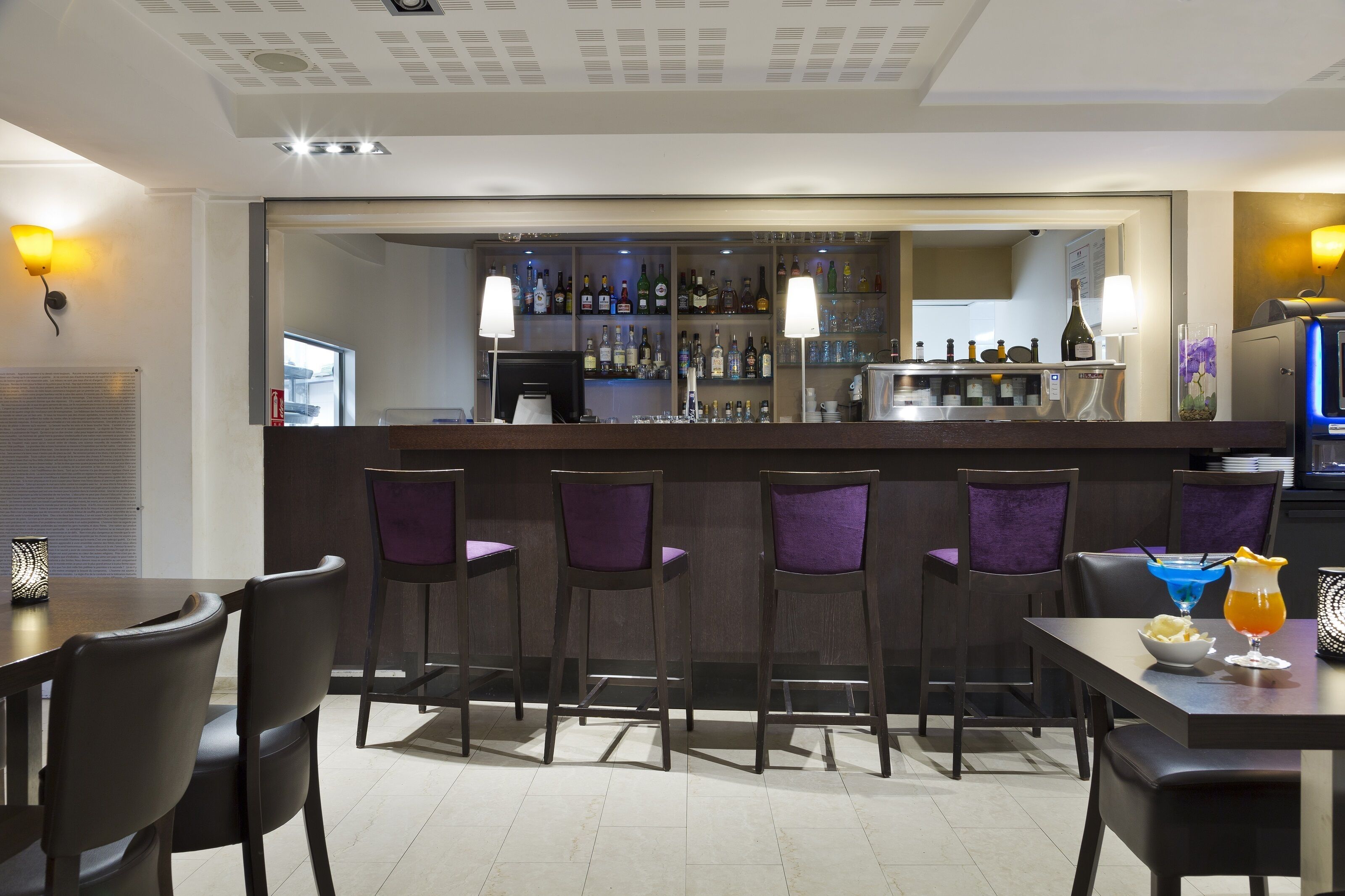 A bar area with a counter, bar stools, and a selection of bottles and glasses.