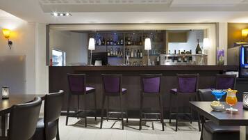 A bar area with a counter, bar stools, and a selection of bottles and glasses.