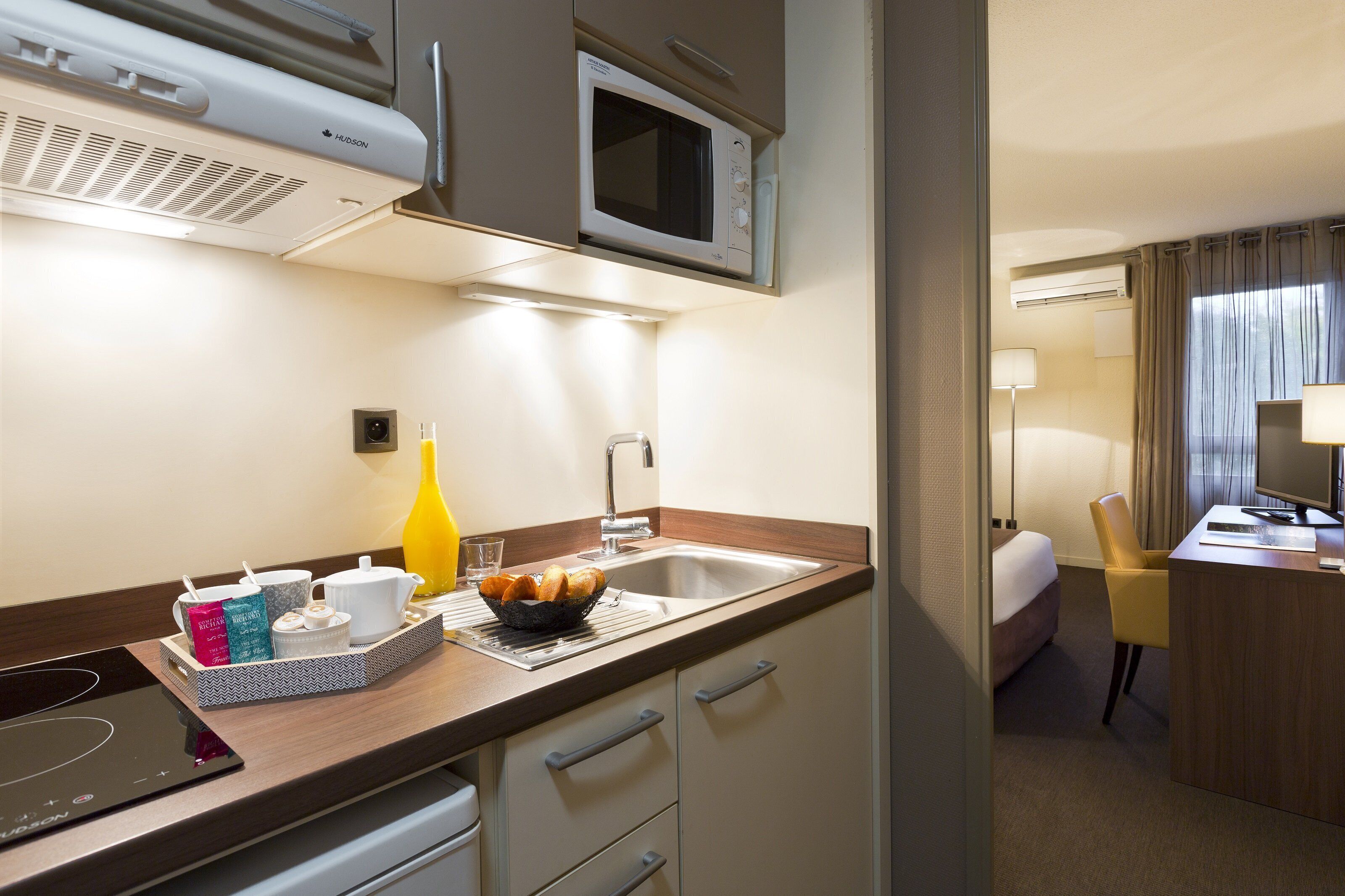 Habitación de hotel con kitchenette, que incluye microondas, lavabo y una pequeña zona de comedor con una bandeja de pan y cafetera.