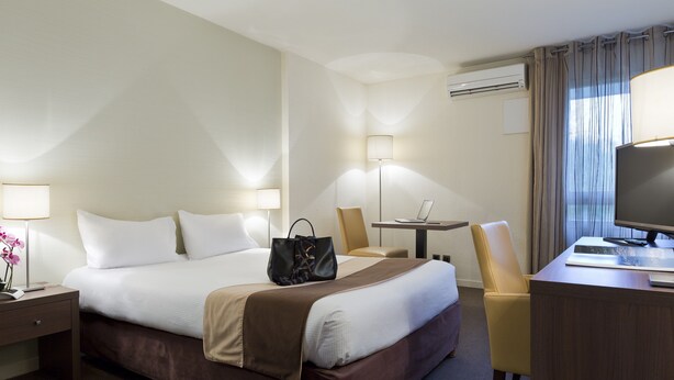 A hotel room with a bed, bedside tables, a desk, a chair, and a TV. - Residence La Reserve (Ferney-Voltaire)