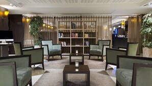 A modern lobby with a central coffee table, seating area, bookshelf, and a television. - Residence La Reserve (Ferney-Voltaire)