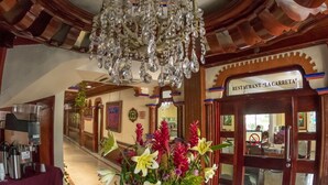 Een lobby met een kroonluchter, een receptiebalie, een bloemstuk en een bord met 'Restaurant La Carreta'.