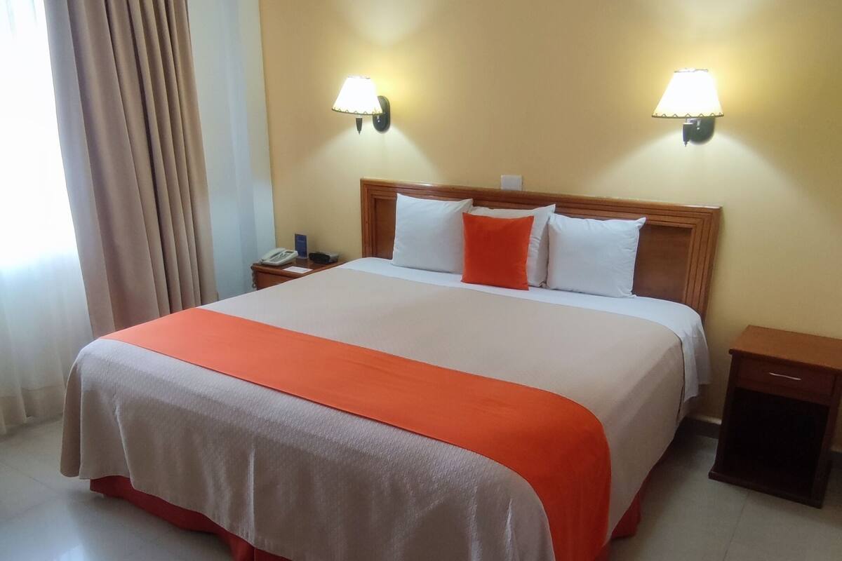 Une chambre d’hôtel avec un grand lit, deux tables de chevet, une petite table et deux lampes fixées au mur.