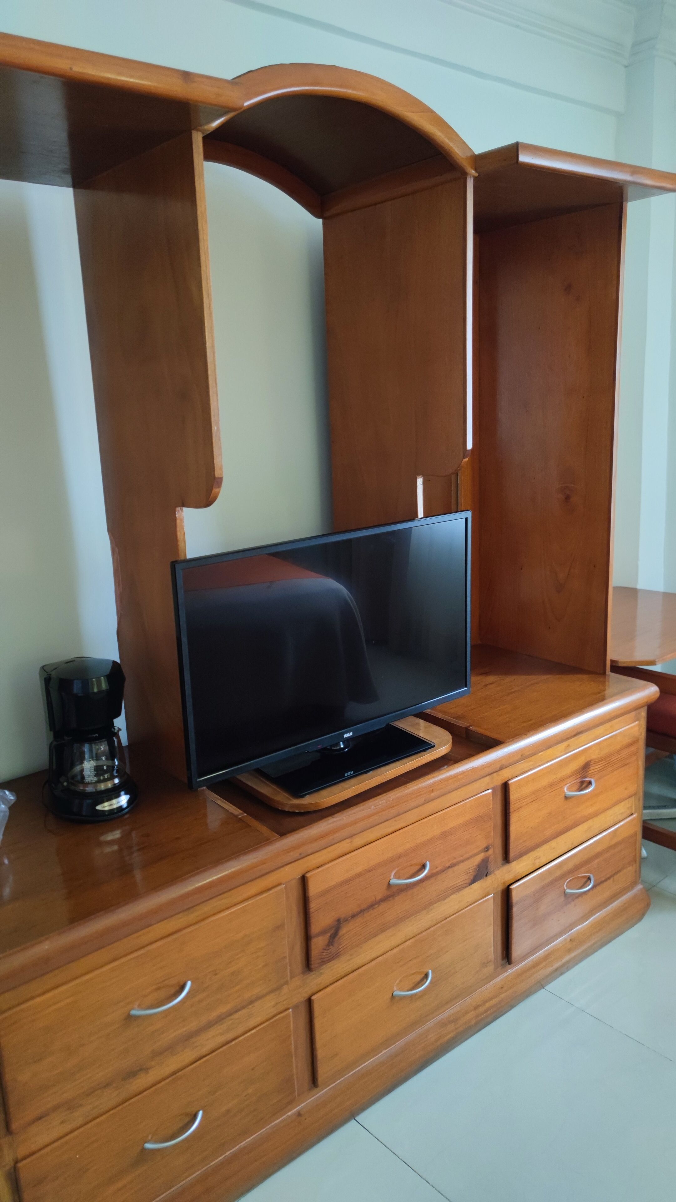 A wooden entertainment center with a flat-screen TV, drawers, and a coffee maker.