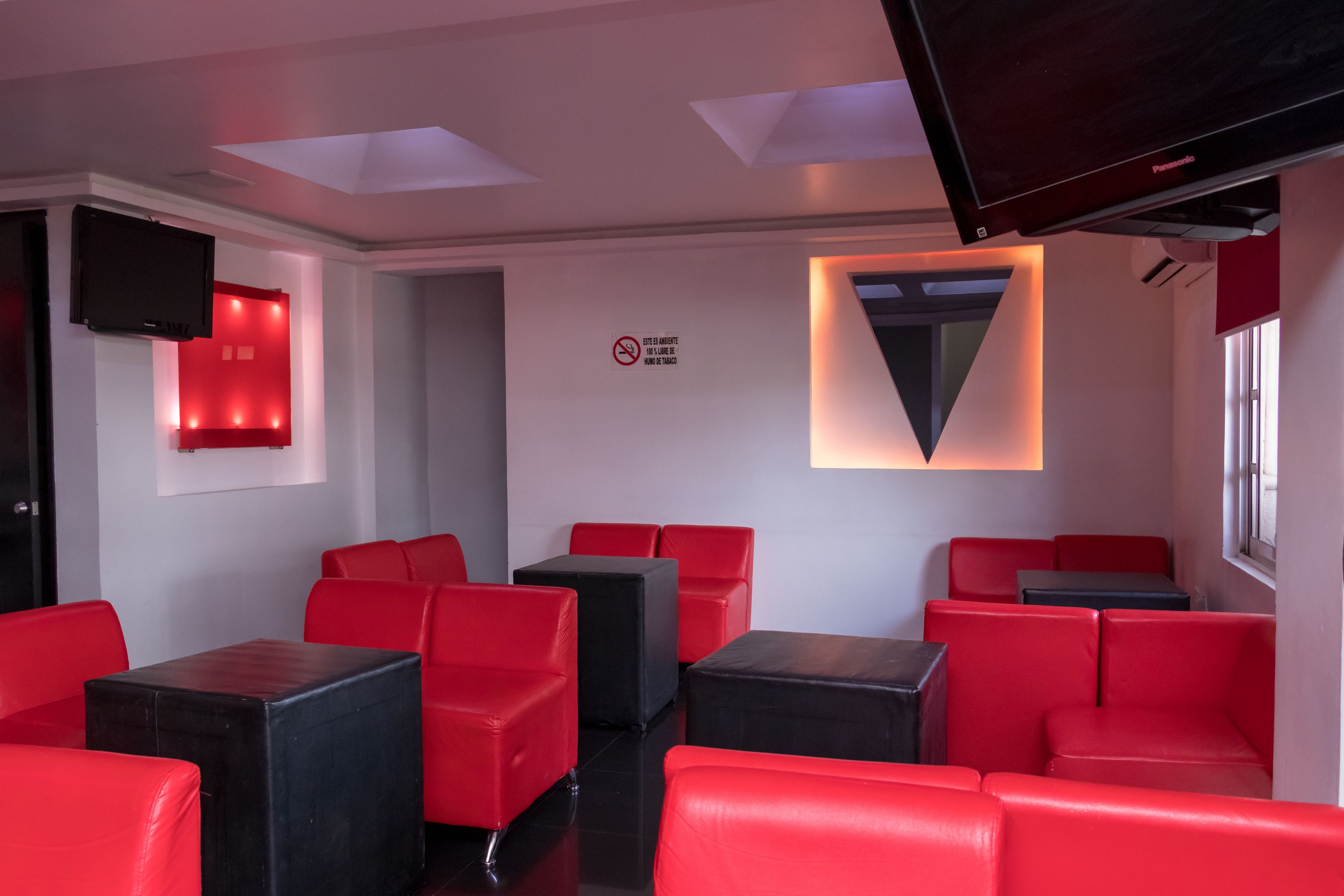 Un intérieur moderne avec des sièges rouges et des tables noires, un téléviseur à écran plat et un panneau indiquant qu'il est interdit de fumer.