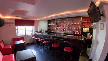 Zona de bar con asientos rojos, una barra con diferentes botellas y un televisor en la pared.