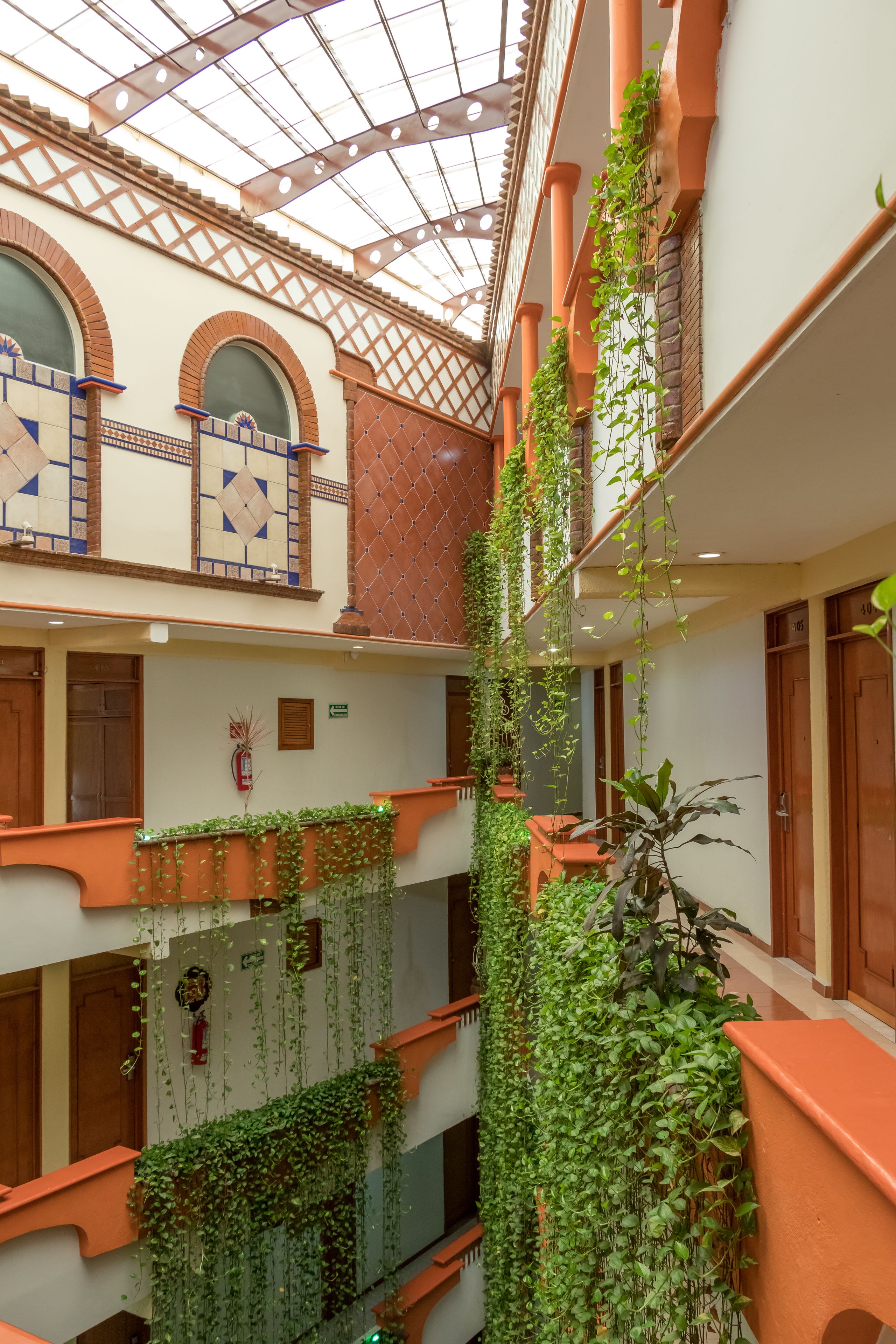 Um átrio em vários níveis com teto de vidro, paredes cor de terracota e plantas trepadeiras verdes.