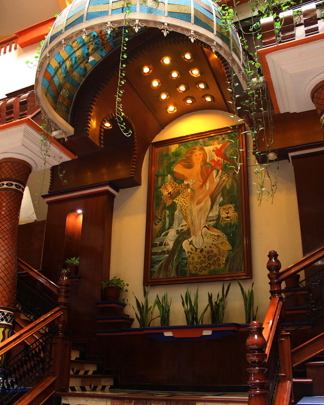 A grand staircase with a wooden handrail, a decorative ceiling, and a painting of a woman with a leopard.