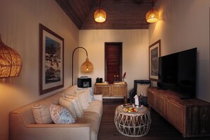 A living room with a sofa, round coffee table, television, wicker side table, and framed artwork on the wall.