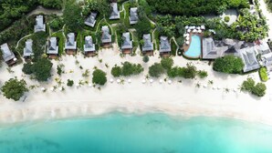 An aerial view of a resort with multiple bungalow-style accommodations, a central swimming pool, and a beachfront.