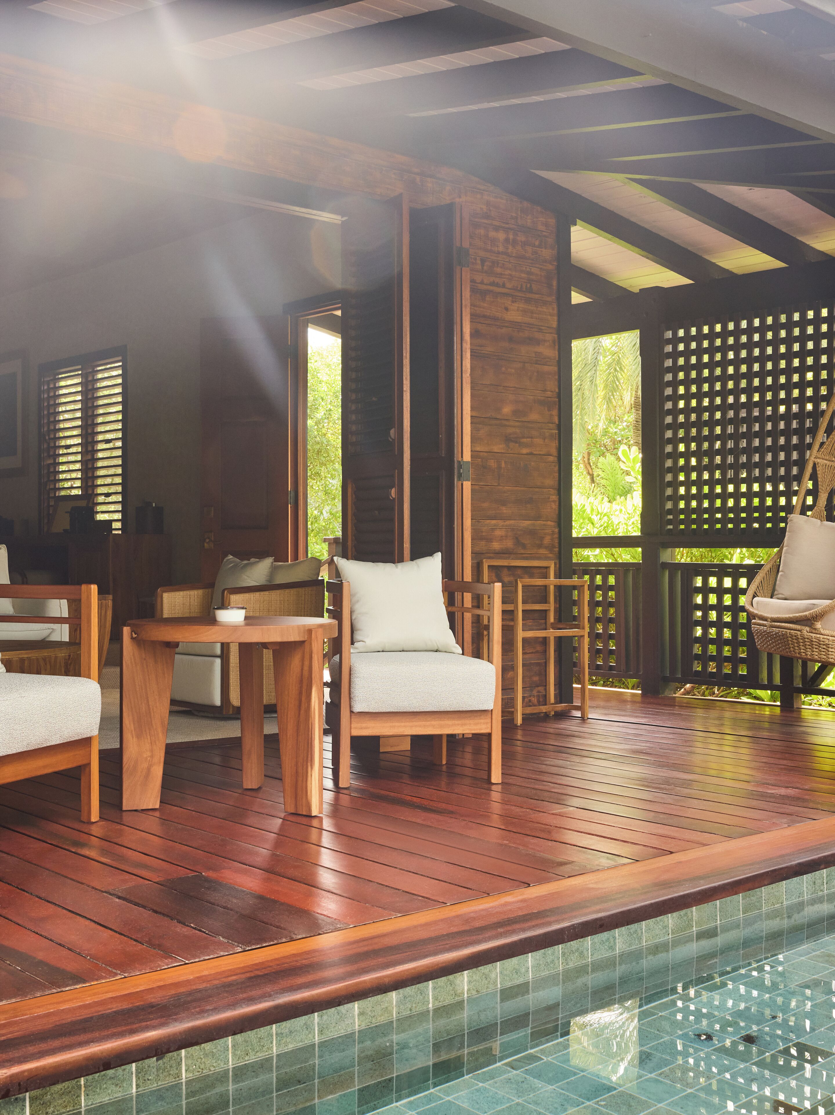 Terraza de madera con piscina, mobiliario de madera y vistas a la vegetación.