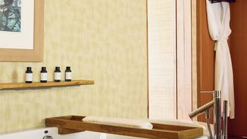 A bathroom with a freestanding bathtub, wooden shelves with bottles, a towel rack with a robe, and a framed picture on the wall.