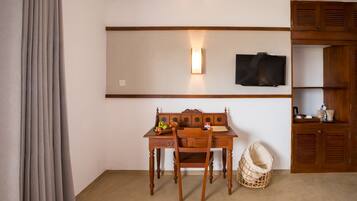 A room with a wooden desk, a chair, a television mounted on the wall, and a wooden wardrobe.