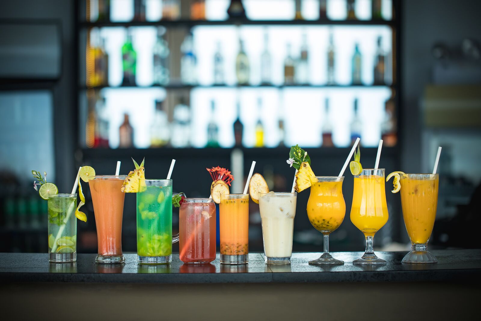 A bar with various colorful cocktails, each garnished with fruits and straws.