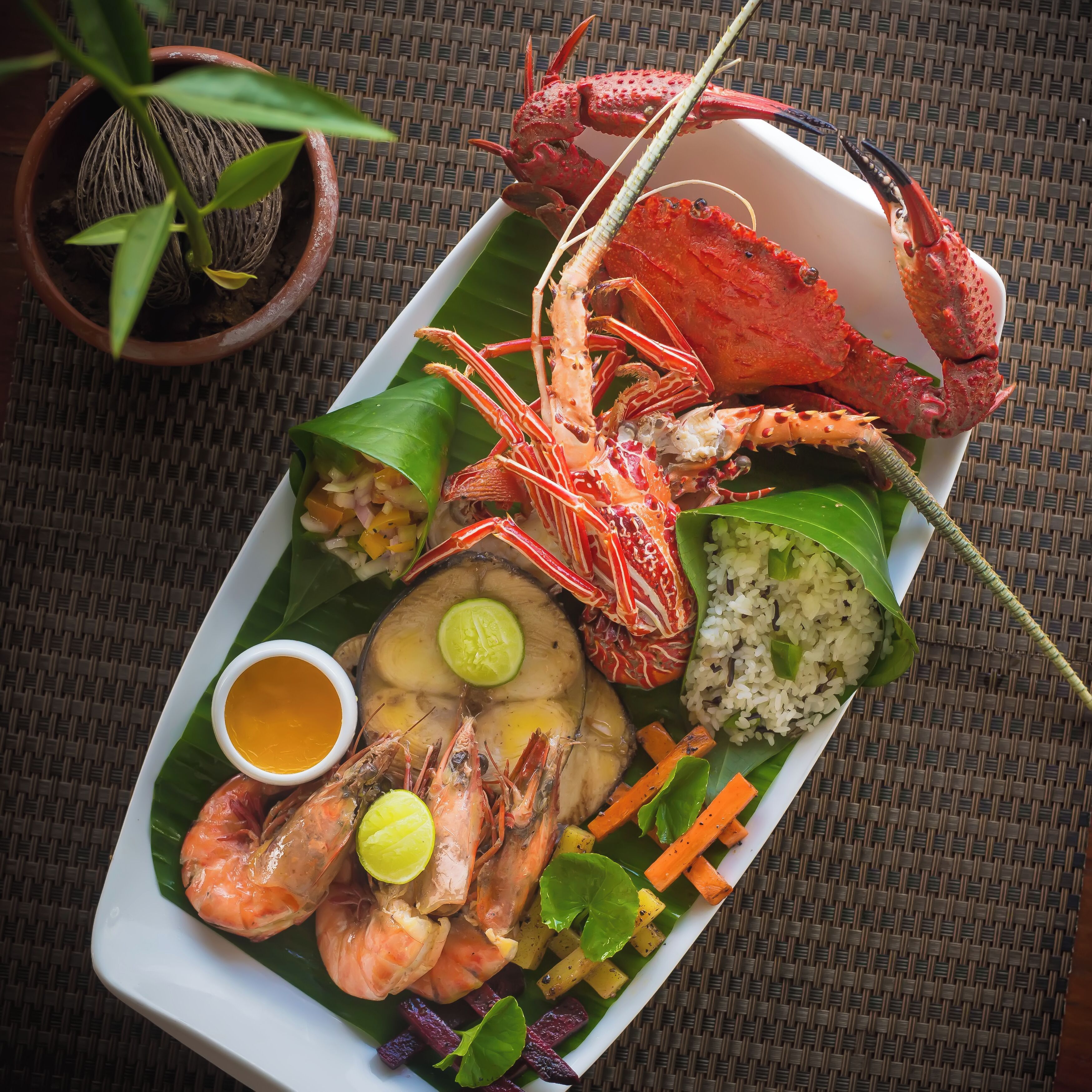 Una bandeja de mariscos con camarones, cangrejo y arroz sobre una hoja de plátano.