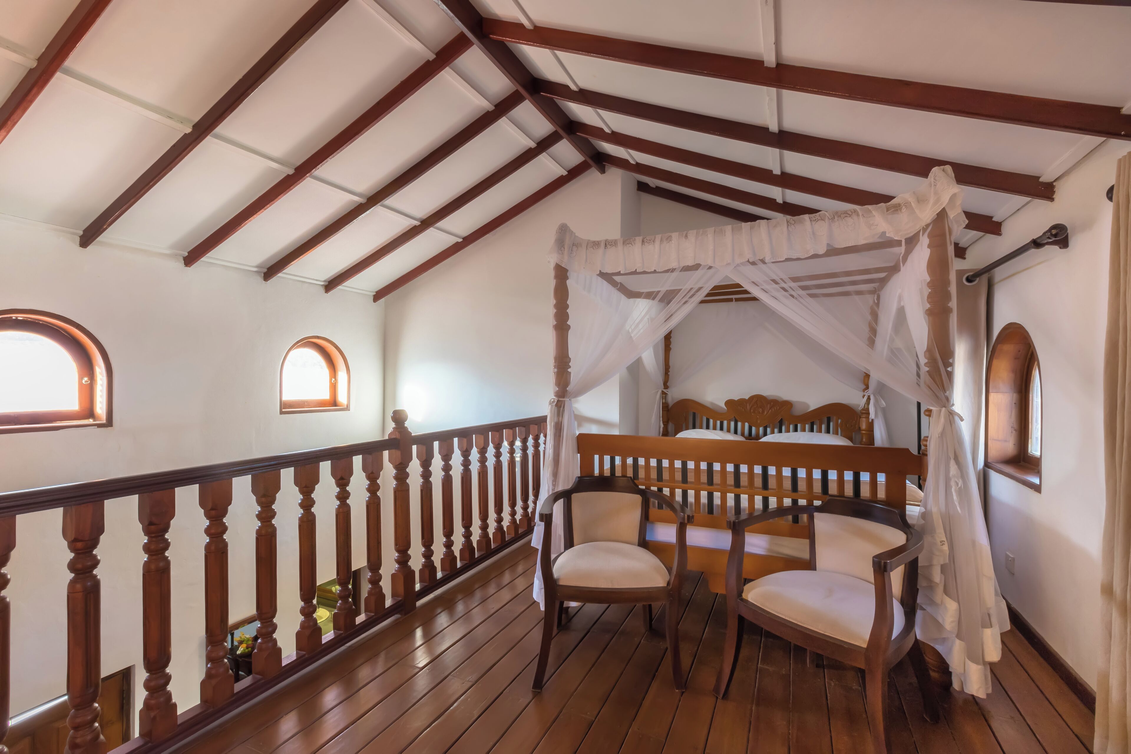 A room with a wooden floor, a four-poster bed, and a balcony with a wooden railing.