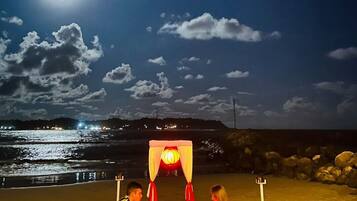 Ein Essbereich am Strand mit einem Tisch unter einer Markise, mit Blick auf das Meer und einen vom Mond erleuchteten Himmel.