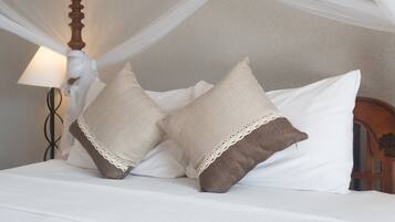 A bed with white bedding and two pillows, one with a lace trim.