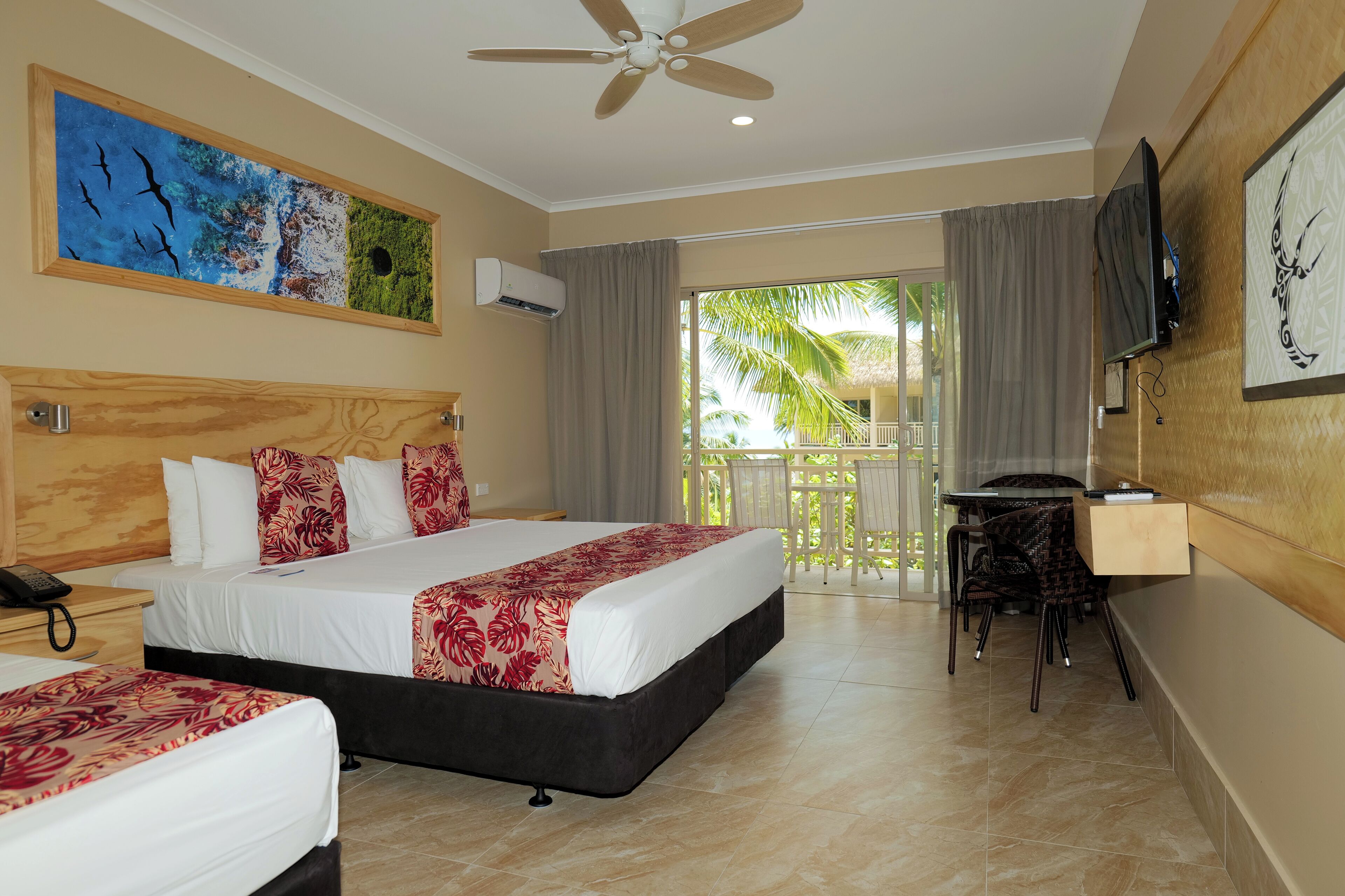 A hotel room with two beds, a ceiling fan, a TV, and a balcony with a view of palm trees.