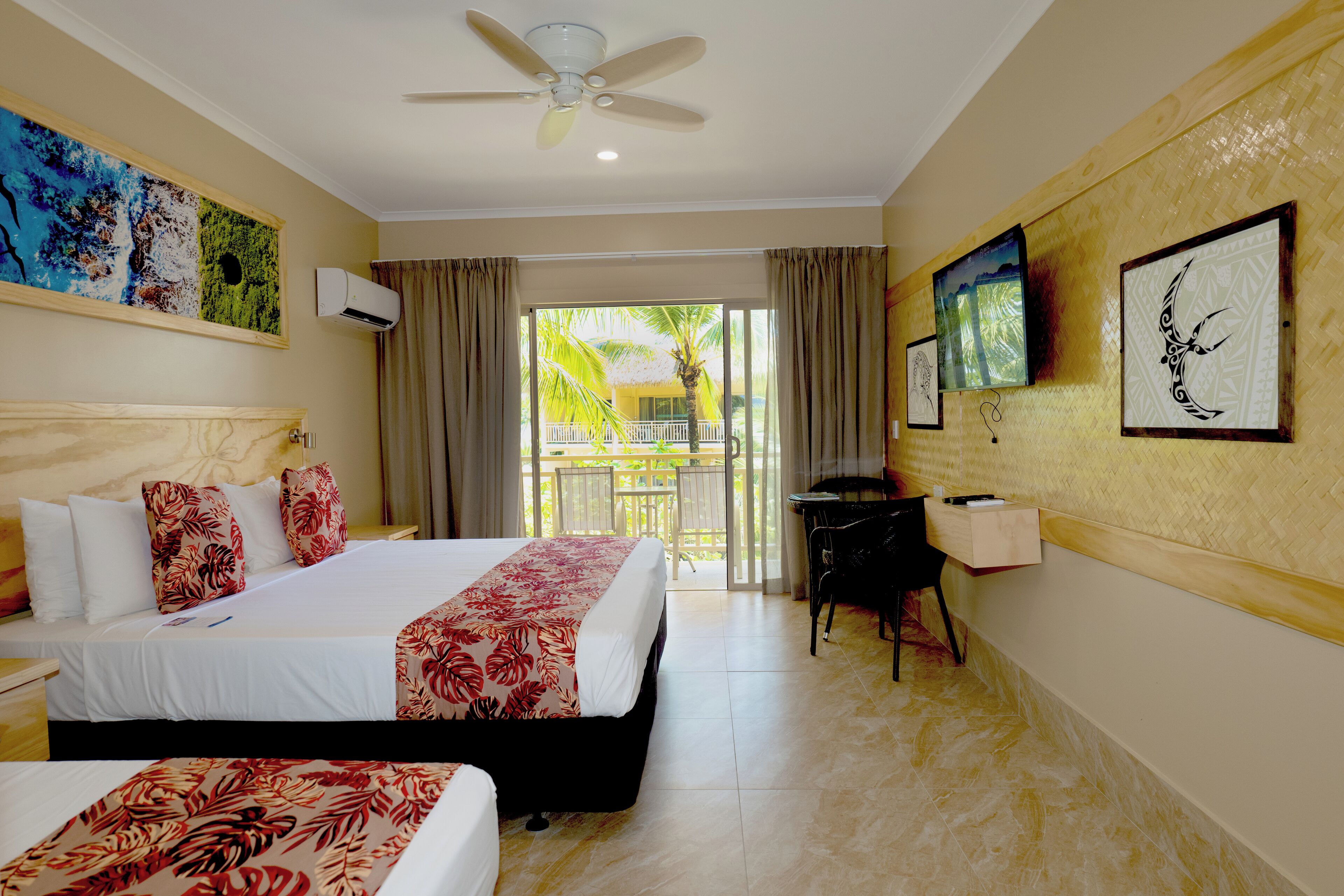 A hotel room with a bed, a desk, a chair, a TV, and a balcony with a view of palm trees.