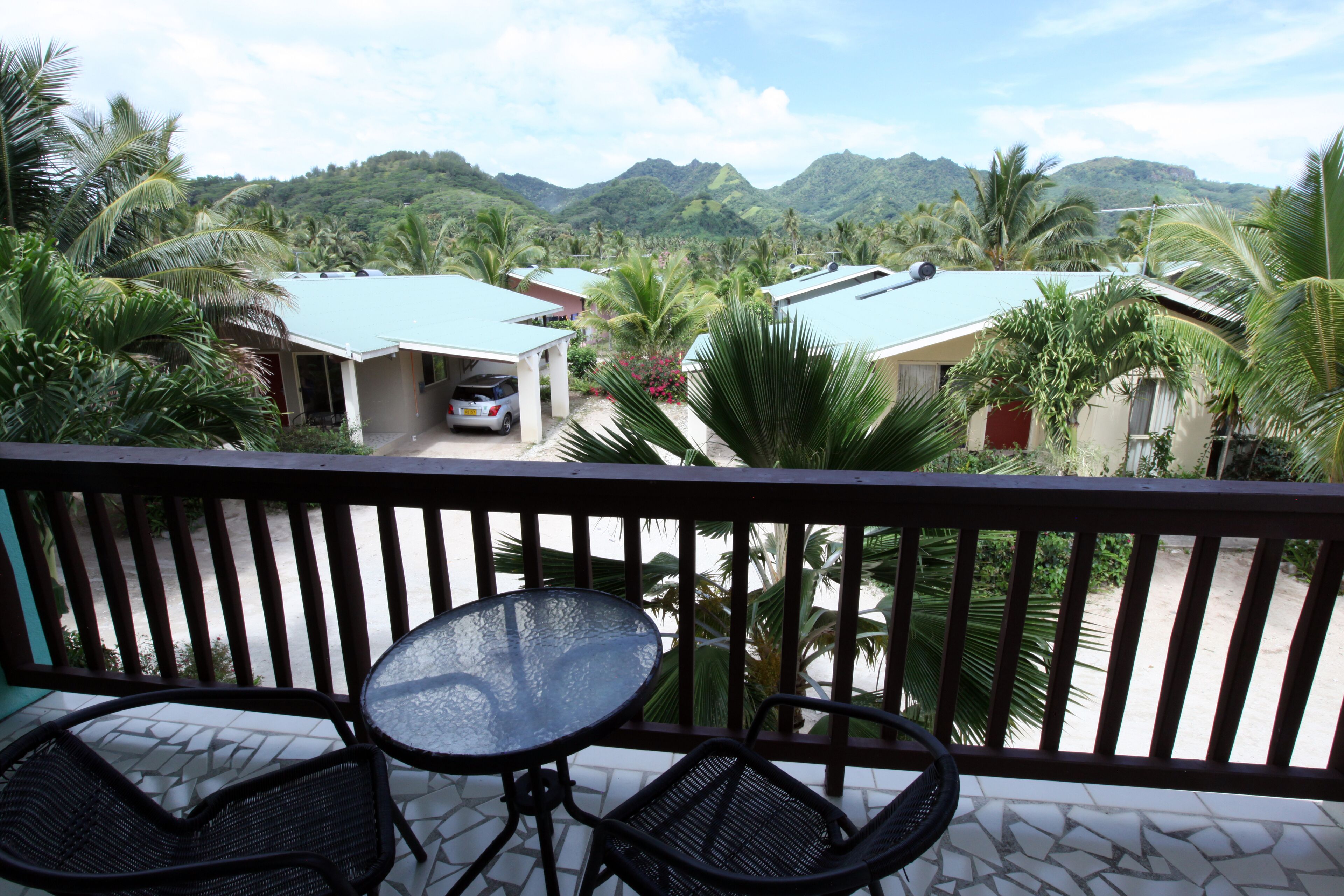 A balcony with a table and two chairs, overlooking a residential area with houses and palm trees.