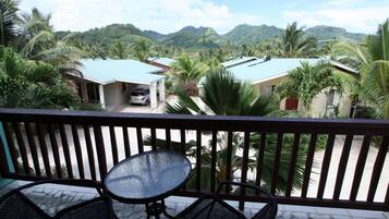 A balcony with a table and two chairs, overlooking a residential area with houses and palm trees.