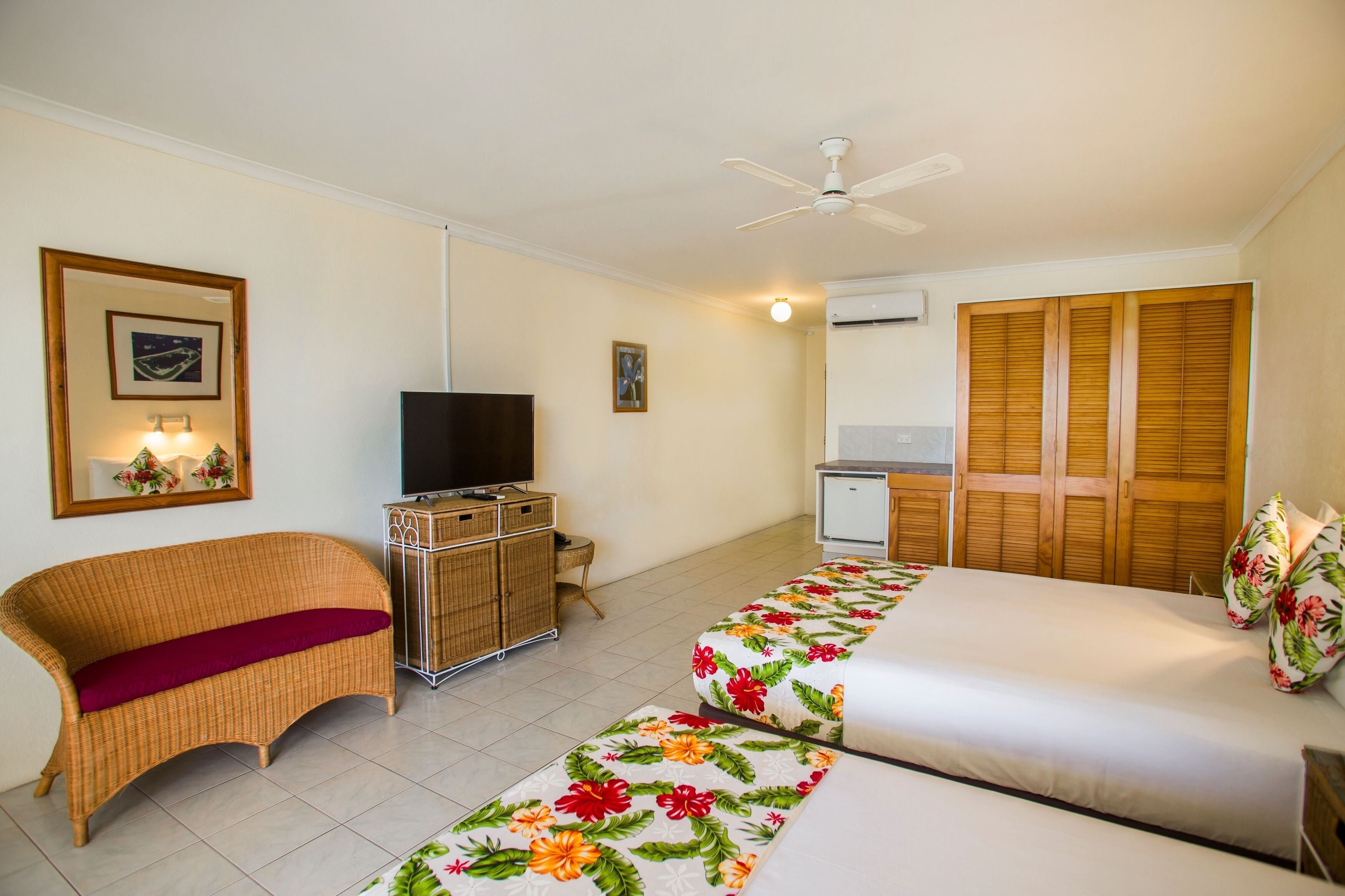 A hotel room with two beds, a television, a wardrobe, and a small desk.