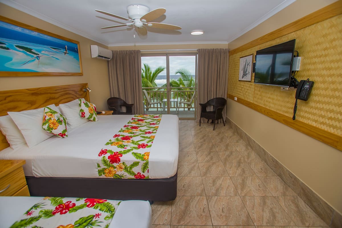 Une chambre d’hôtel comprenant un lit, un bureau, une chaise, une télévision et un balcon avec vue sur l’océan.