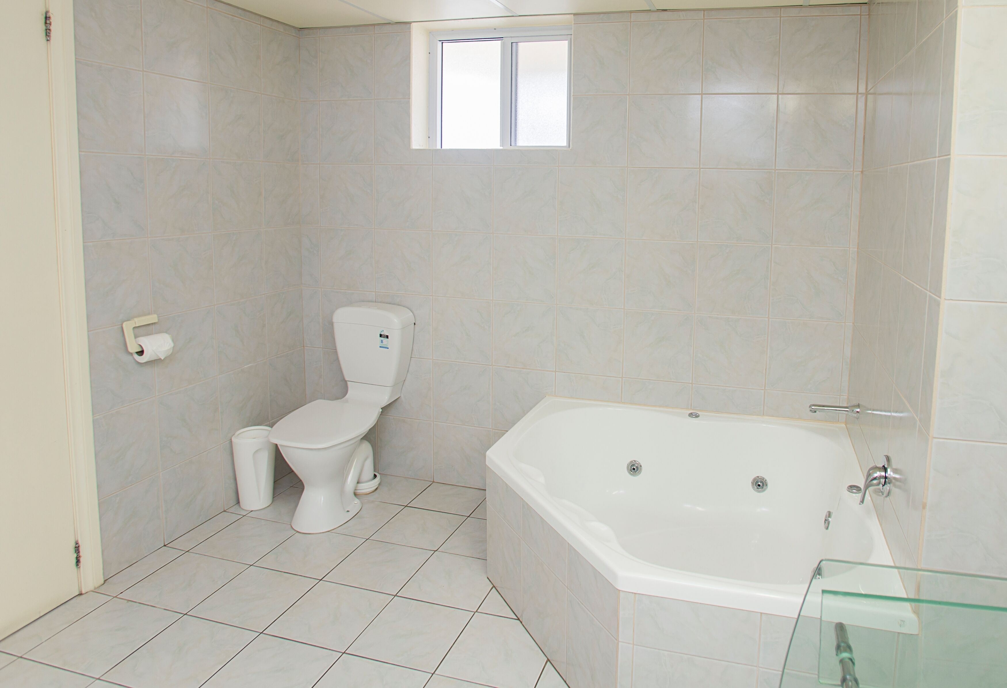 Een badkamer met een toilet, een badkuip en een klein raam.