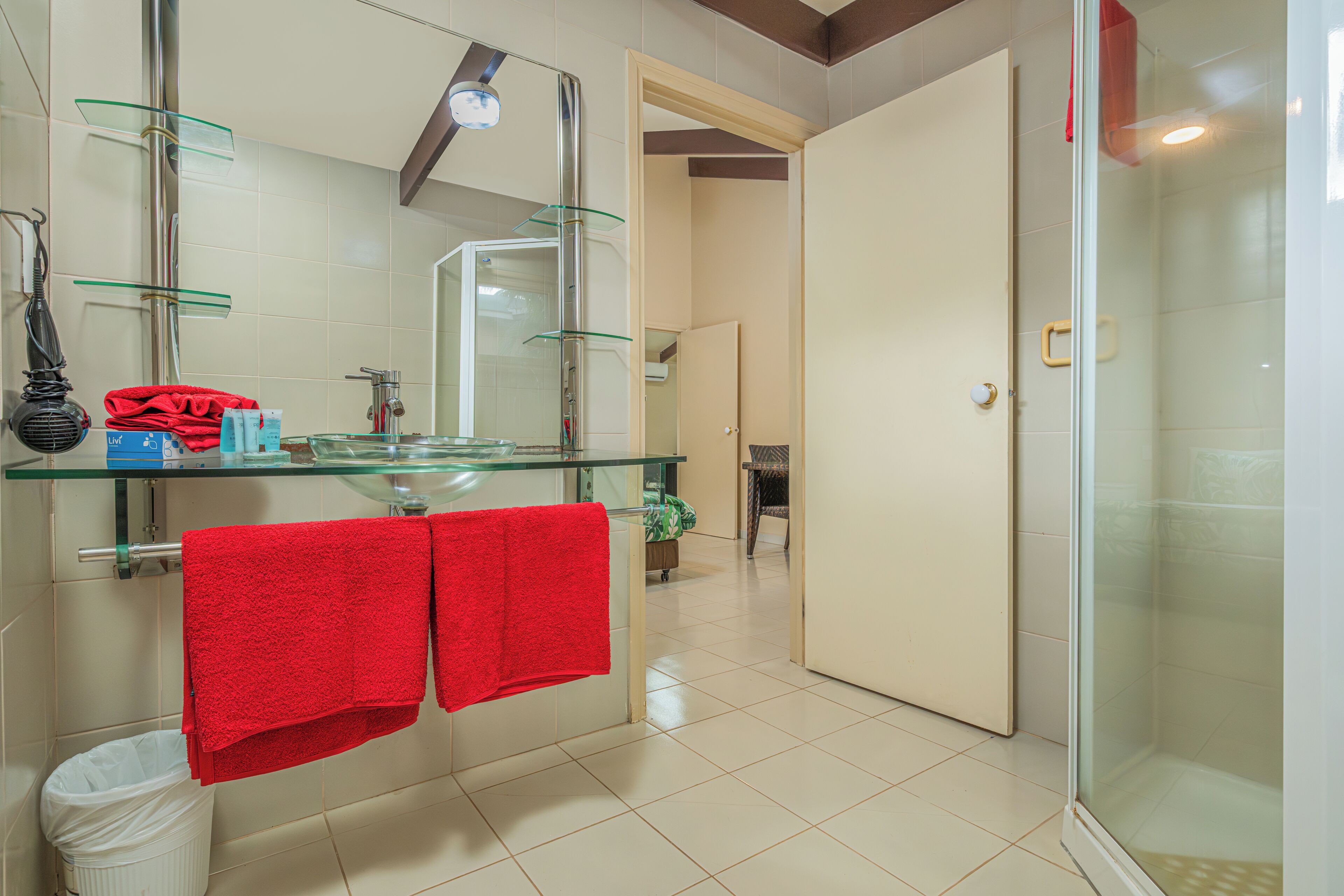 A modern bathroom with a glass shower enclosure, a glass sink, and a red towel hanging on the wall.